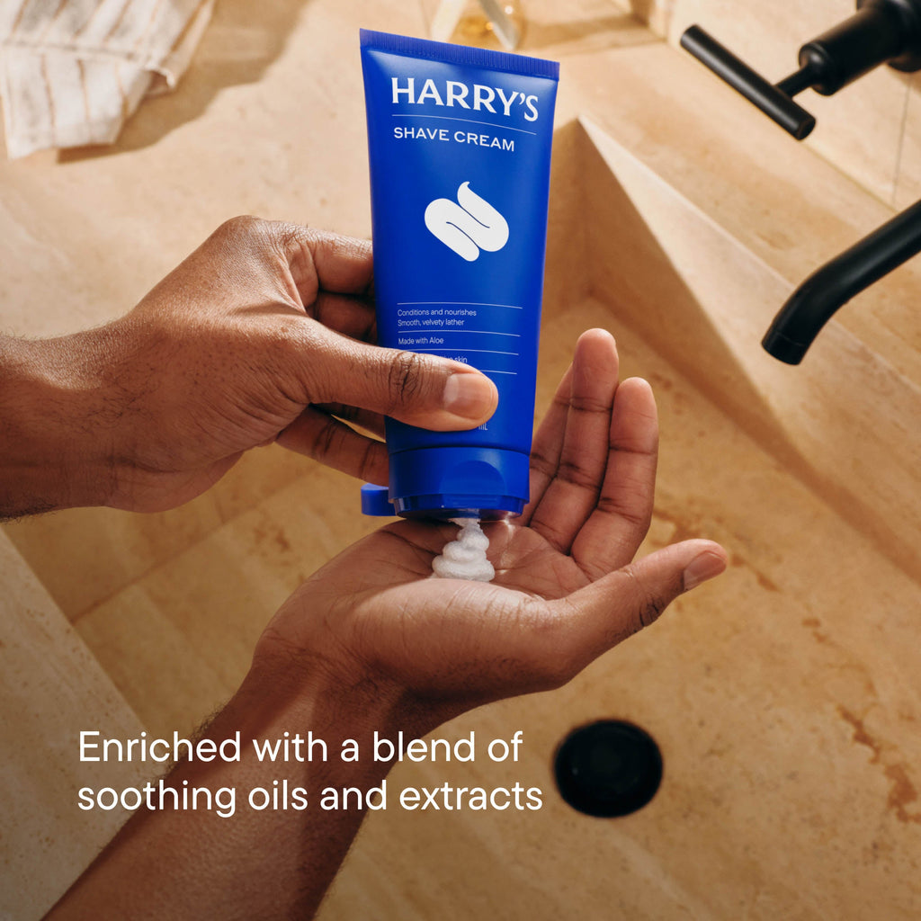 Hand holding a tube of Harry's Shave Cream with a bathroom background