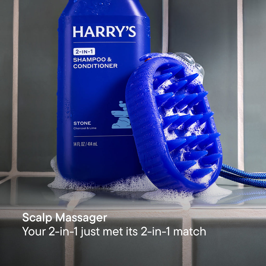 Blue bottle of 'HARRY'S' 2-in-1 Shampoo & Conditioner with a scalp massager on a gray surface.