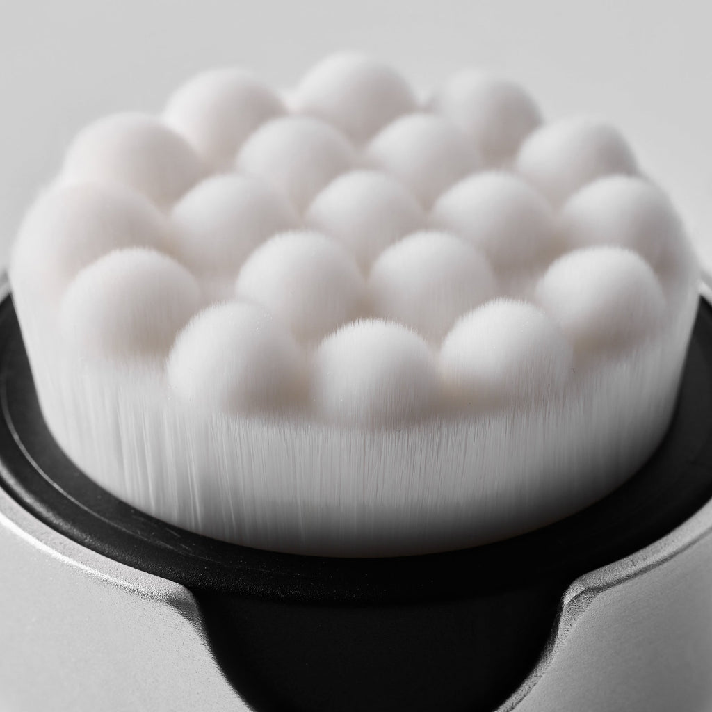 Close-up of a white cleansing brush with bristles on a gray background