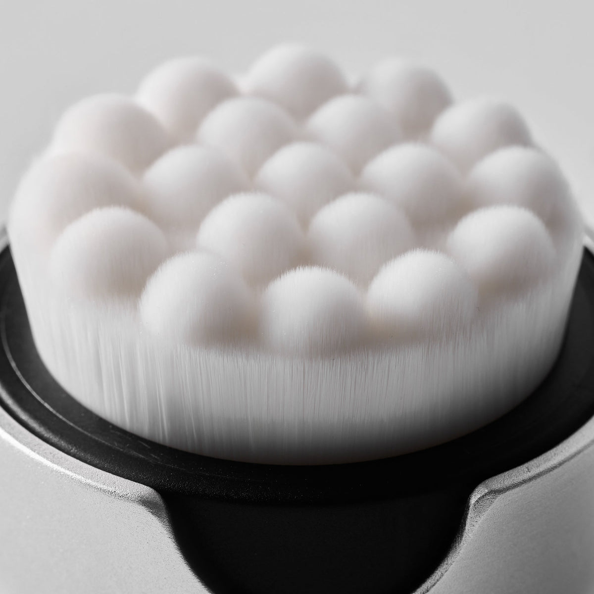 Close-up of a white cleansing brush with bristles on a gray background