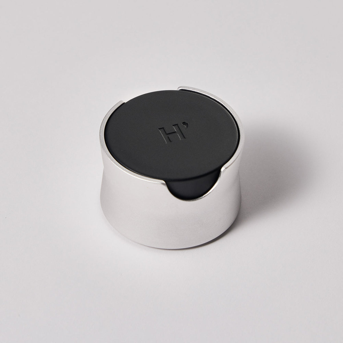 Round metallic face wash brush with black top on a light gray background