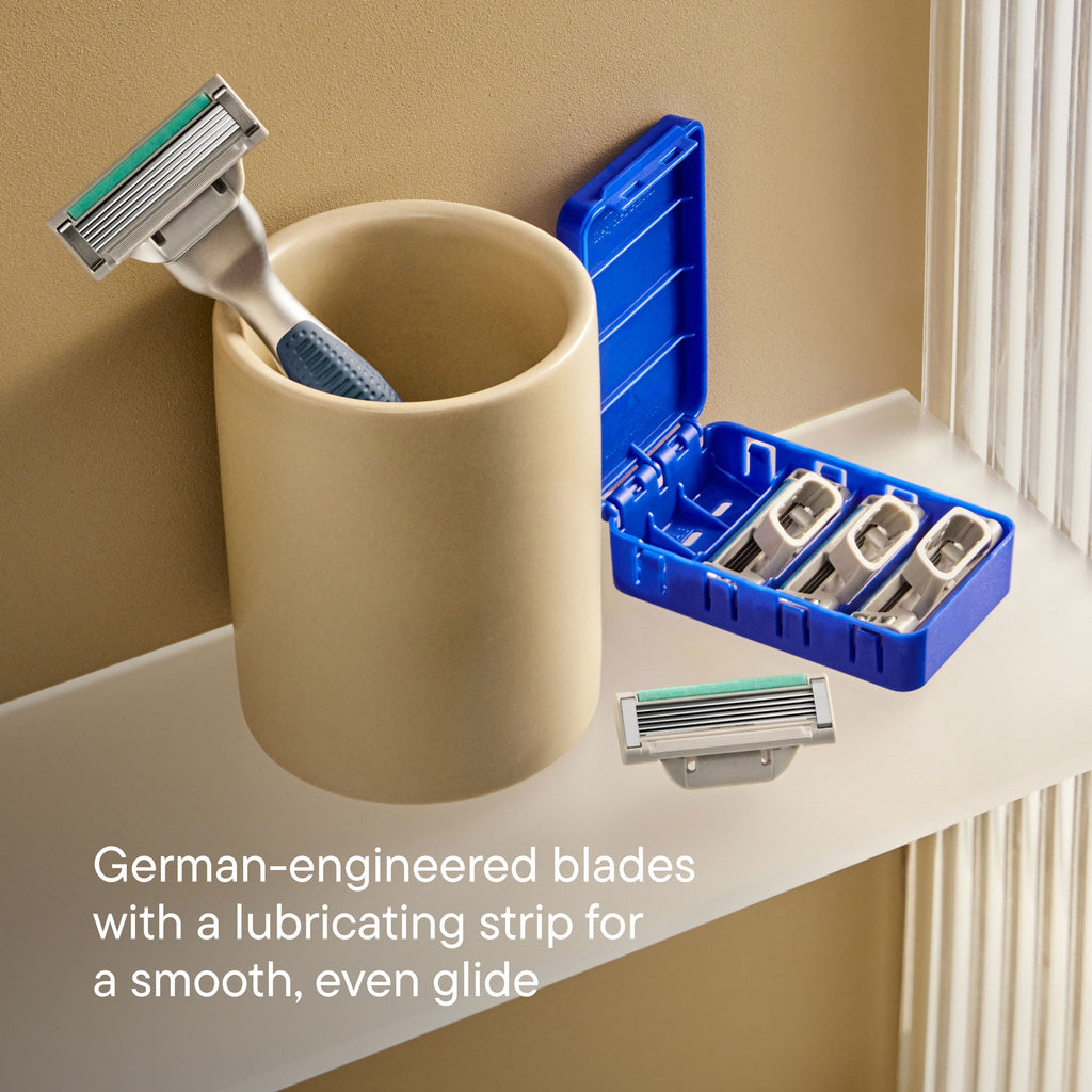 Beige cup with razors, blue razor holder with additional blades on a bathroom counter.