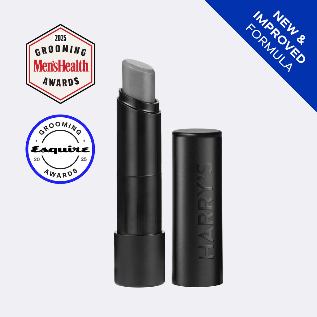 A black cosmetic tube and its matching cap on a light gray background, with a silver-gray product bullet visible. The cap is embossed with the brand name HARRY'S.