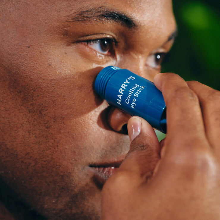 Person applying a blue cooling eye stick labeled 'Harry's' to their under eye.
