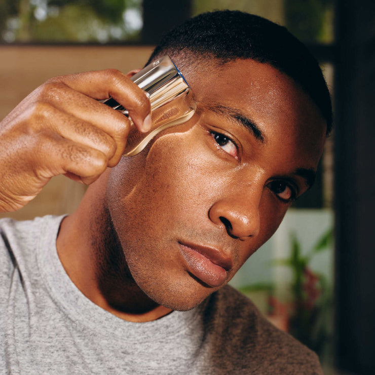 Man using a facial massage tool on his face, wearing a gray shirt.