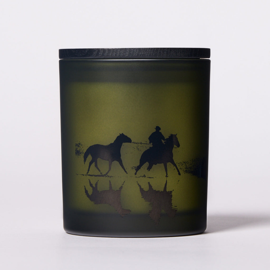 Candle with horse design on a black lid and base.
