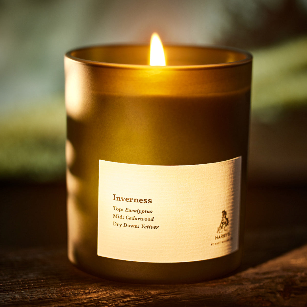 Candle labeled 'Inverness' with a label detailing fragrance notes, on a wooden surface.