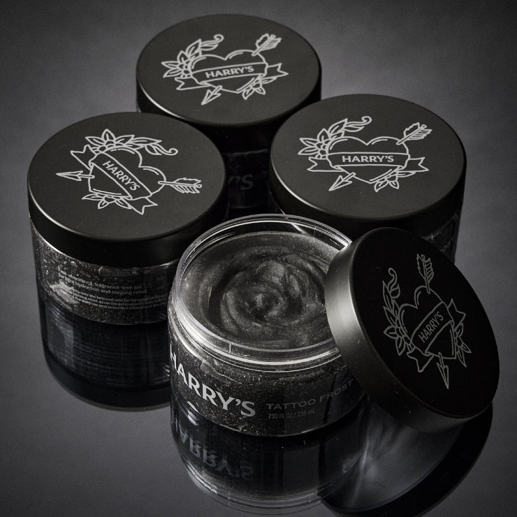 4 jars of 'Harry's' tattoo aftercare product with black lids on a dark background