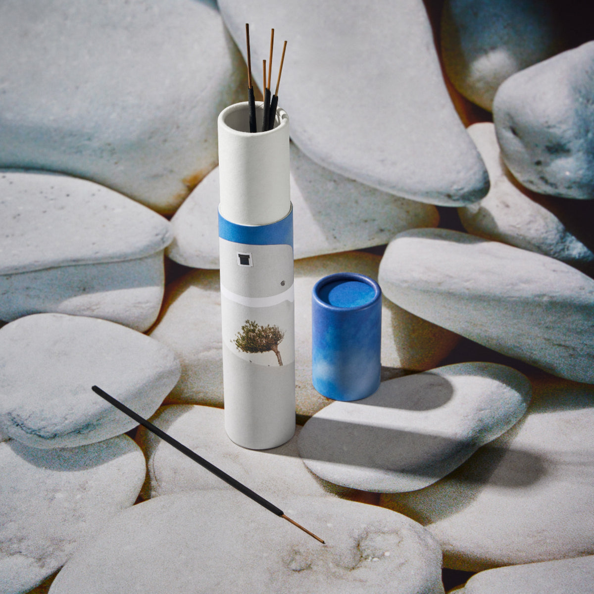 Incense in its white tubular packaging with stones in the background.