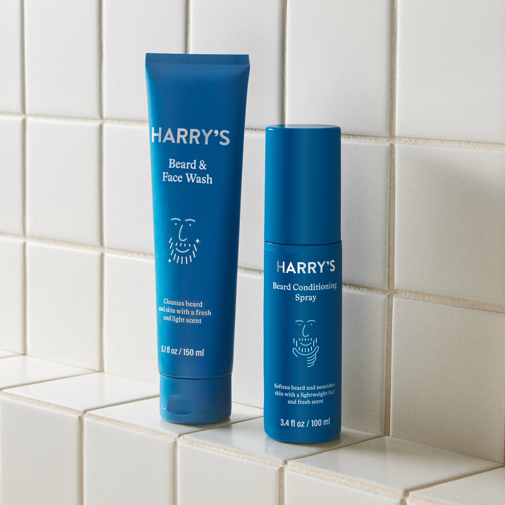 Two blue bottles of 'Harry's' beard care products on a tiled surface.