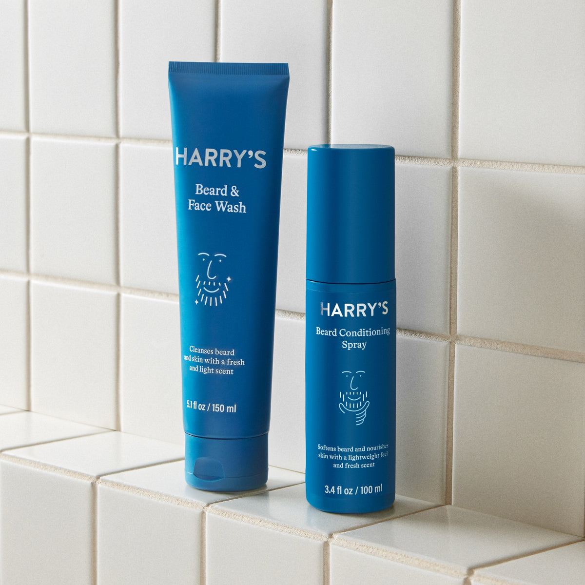 Two blue bottles of 'Harry's' beard care products on a tiled surface.