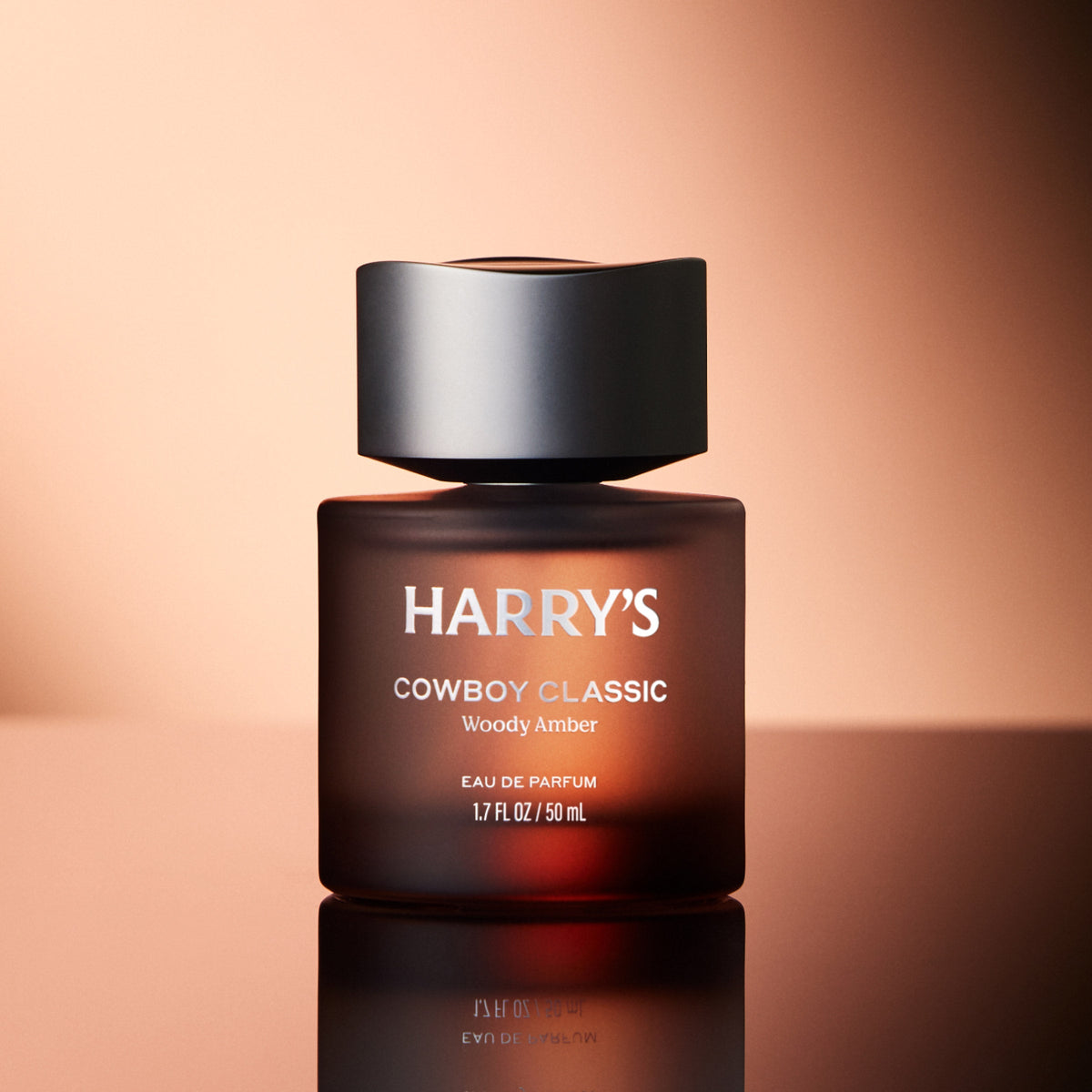Harry's Cowboy Classic Woody Amber eau de parfum bottle on a reflective surface with a warm background