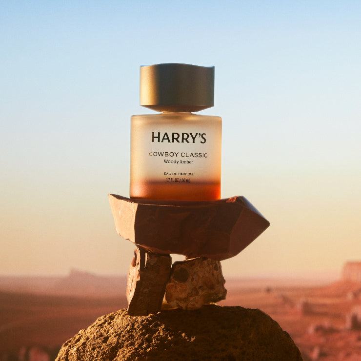 Cologne bottle labeled 'Harry's Cowboy Classic' on a rock with a desert landscape in the background