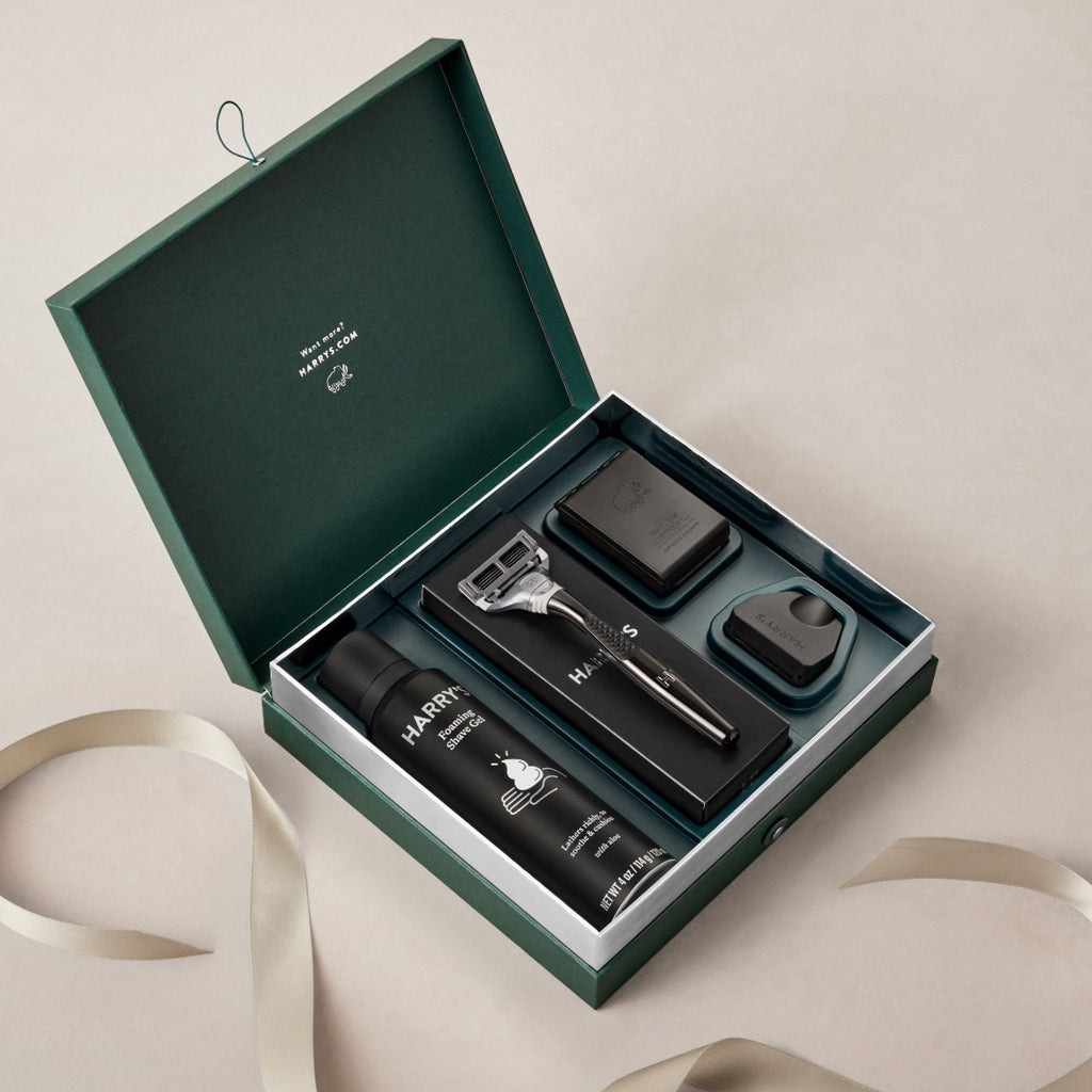 Grooming kit with razor, bottles, and other items in a green box on a beige background
