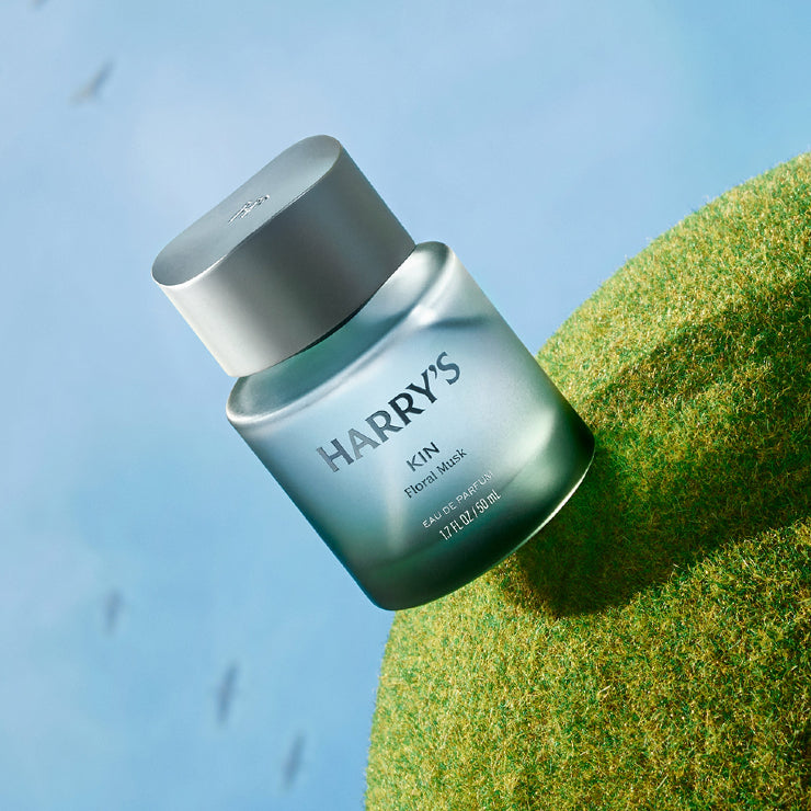 Harry's cologne product on a textured green surface with a blue gradient background