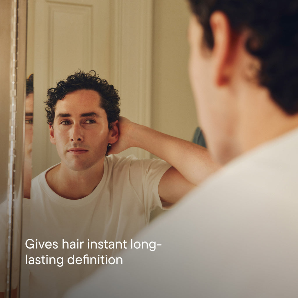 Man looking at his reflection in a mirror with text 'Gives hair instant long-lasting definition'.