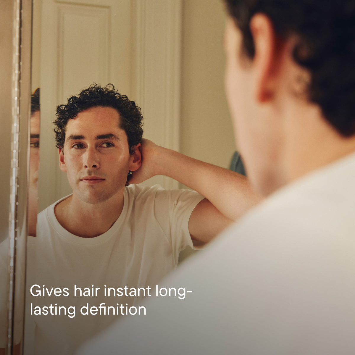 Man looking at his reflection in a mirror with text 'Gives hair instant long-lasting definition'.