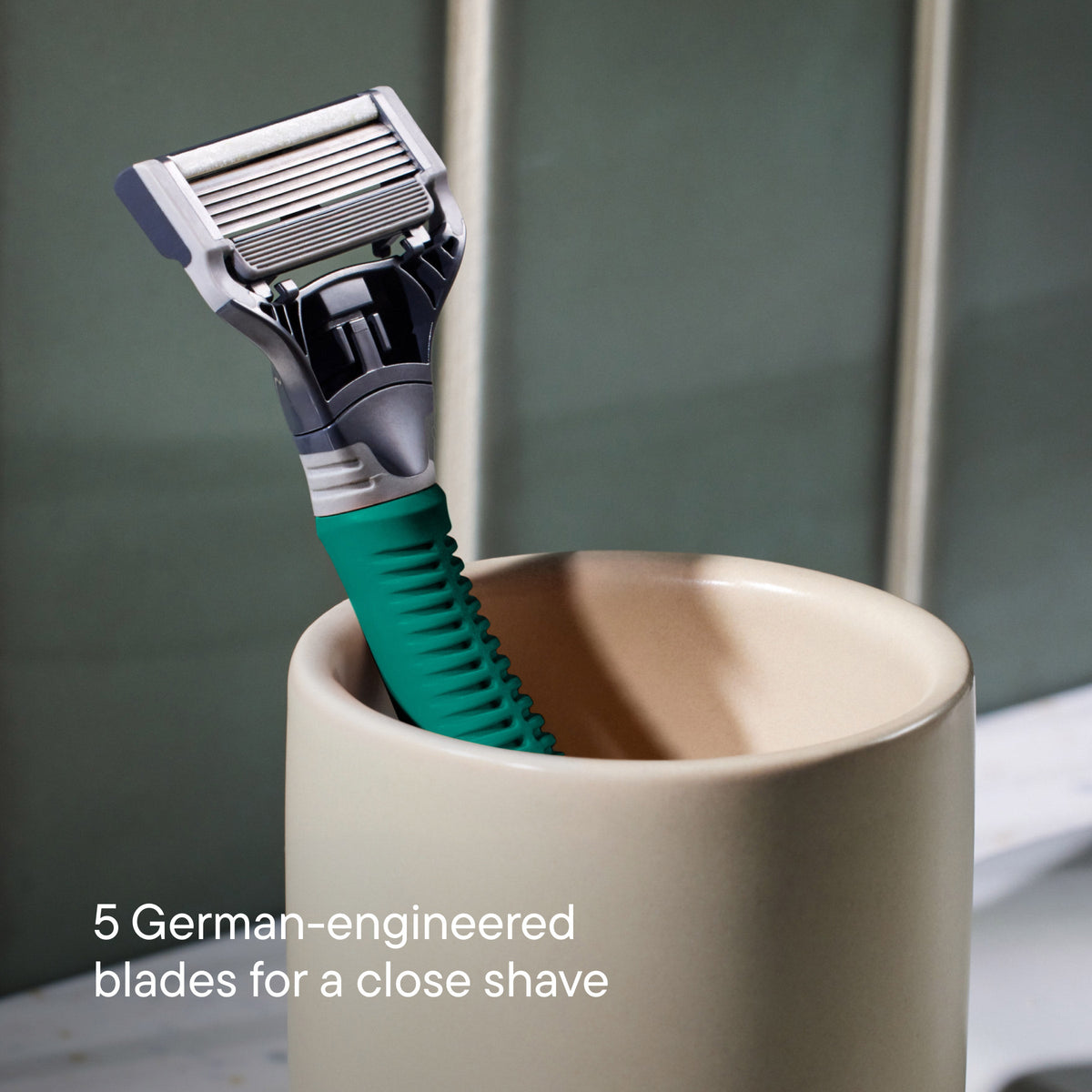 Green Truman razor resting in an off white ceramic cup.