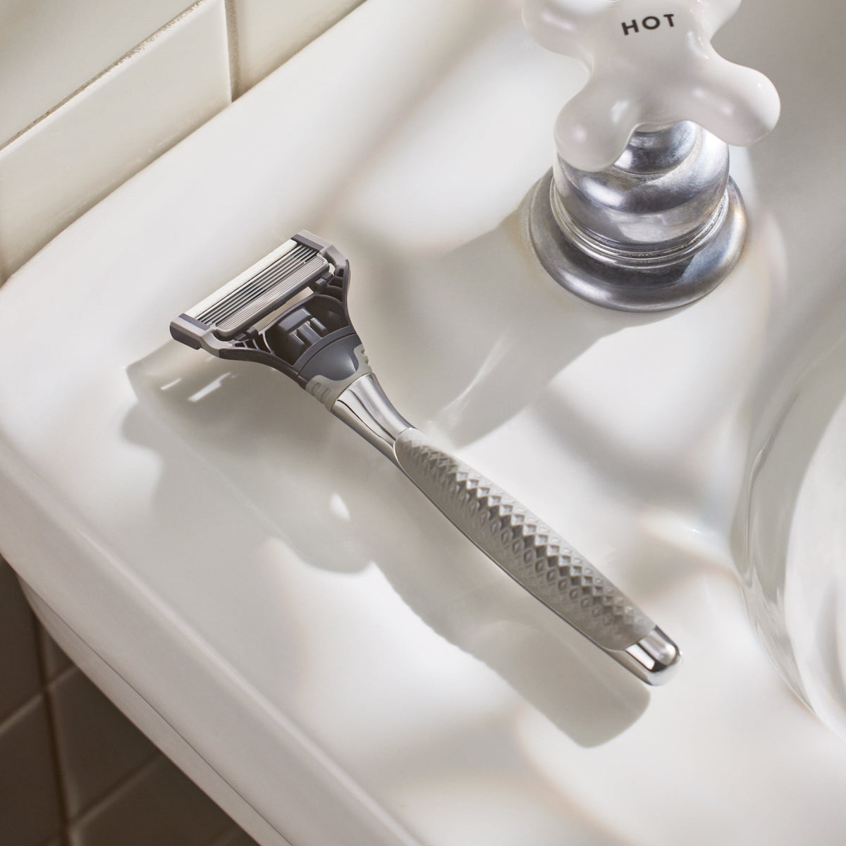 Silver safety razor on a white bathroom counter with a faucet in the background