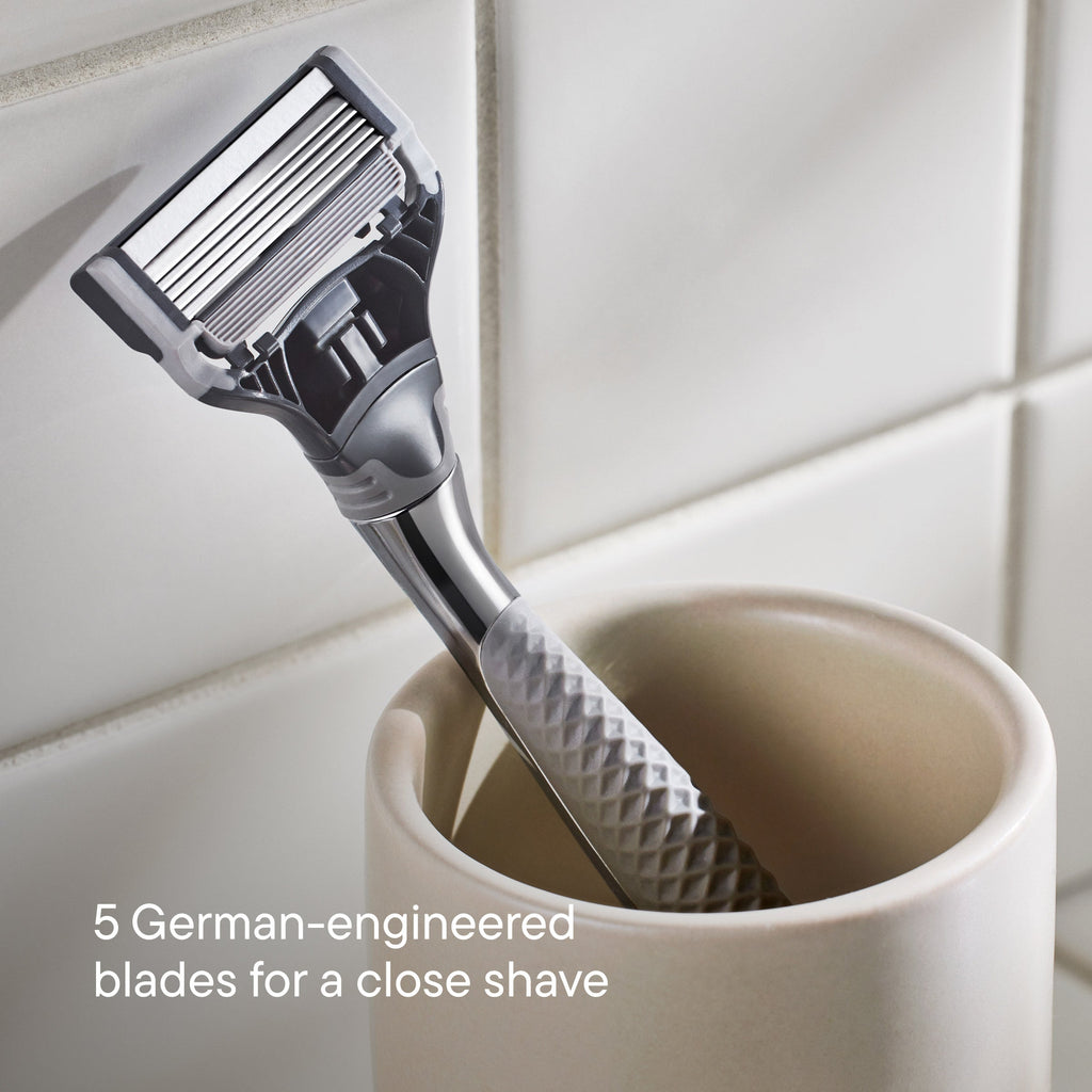 Shaving razor with a textured handle in a white cup against a tiled bathroom wall.