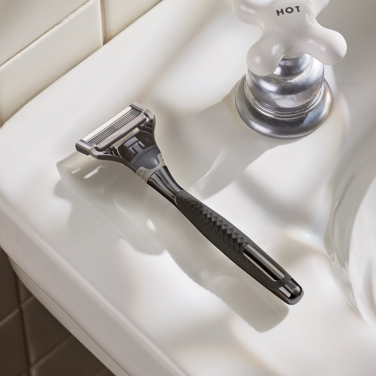 Shaving razor on a bathroom sink with a faucet in the background
