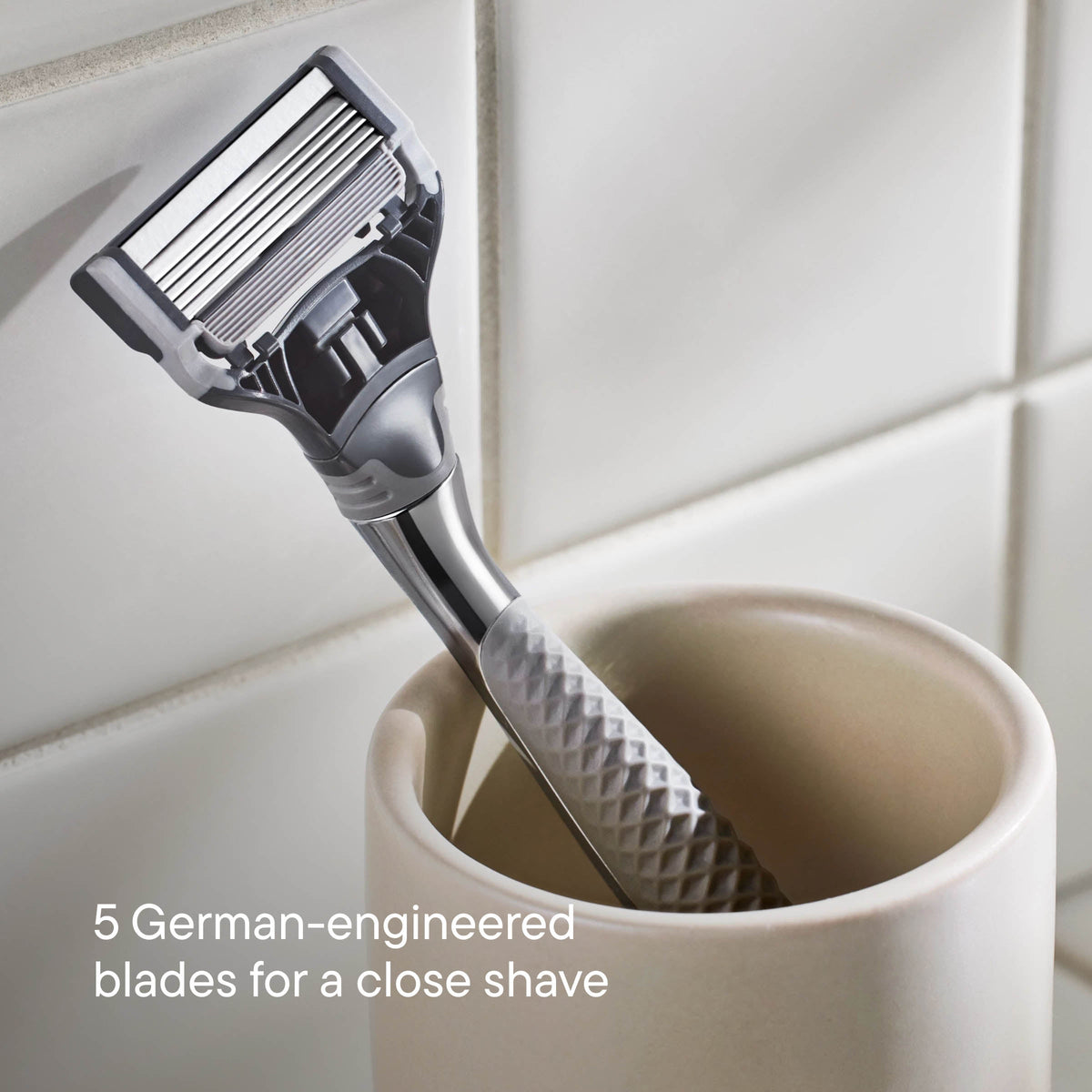 Shaving razor with textured handle in a white cup against a tiled bathroom wall.