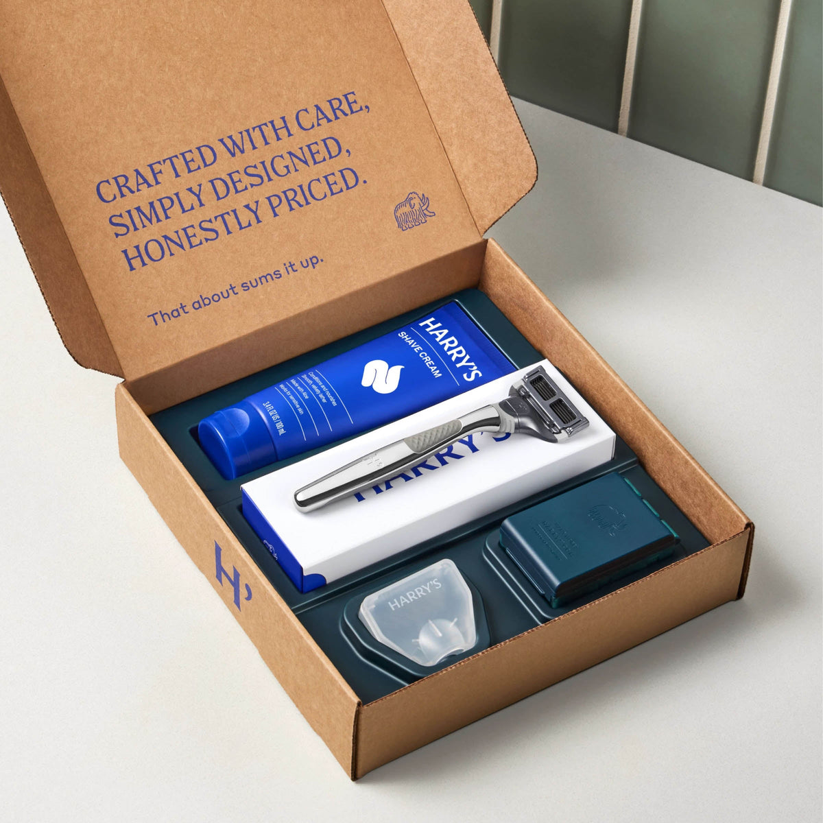 Harry's grooming kit with shaving cream, razor, and other items in a cardboard box on a white surface.