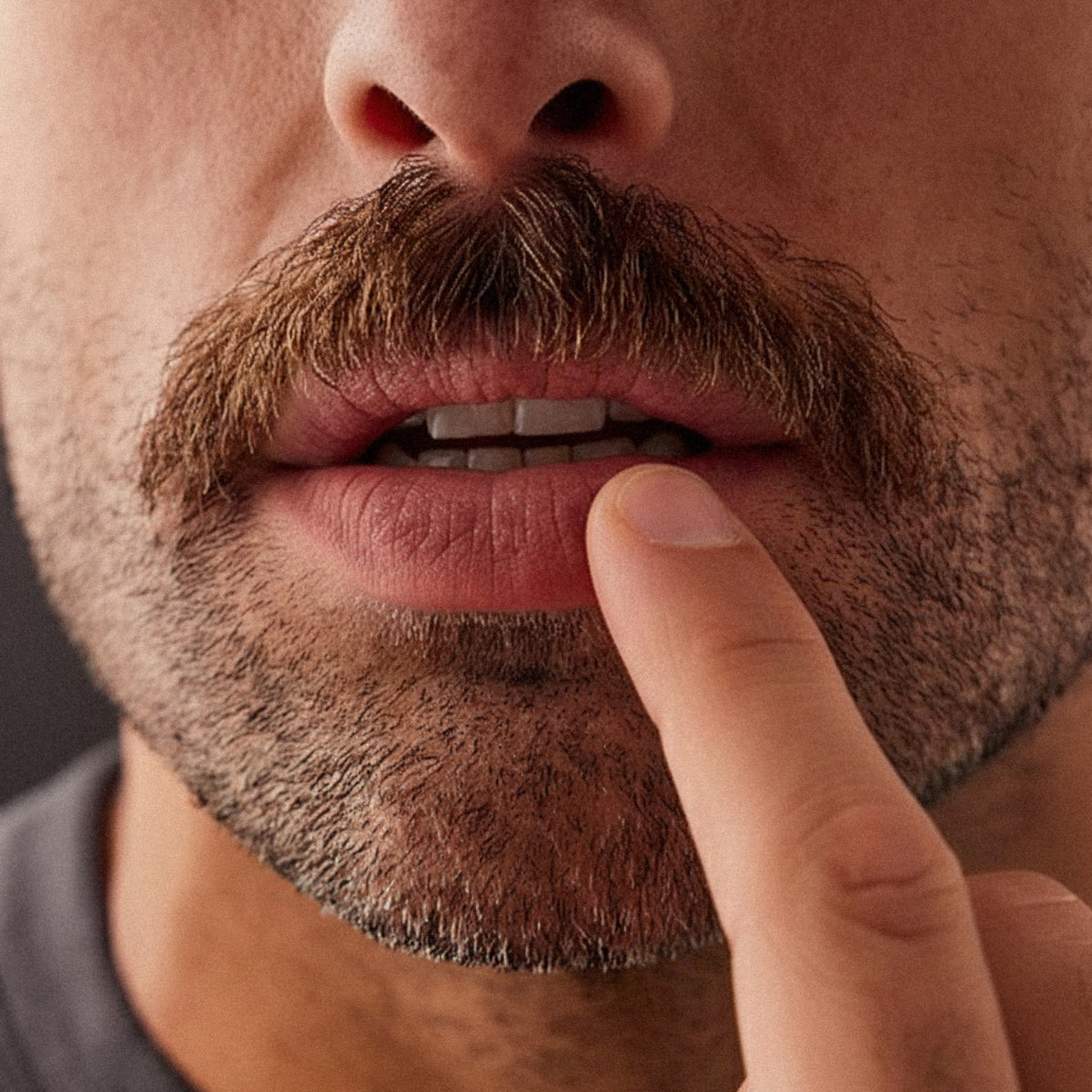 Close-up of a man with a mustache applying product to his lips with a finger.