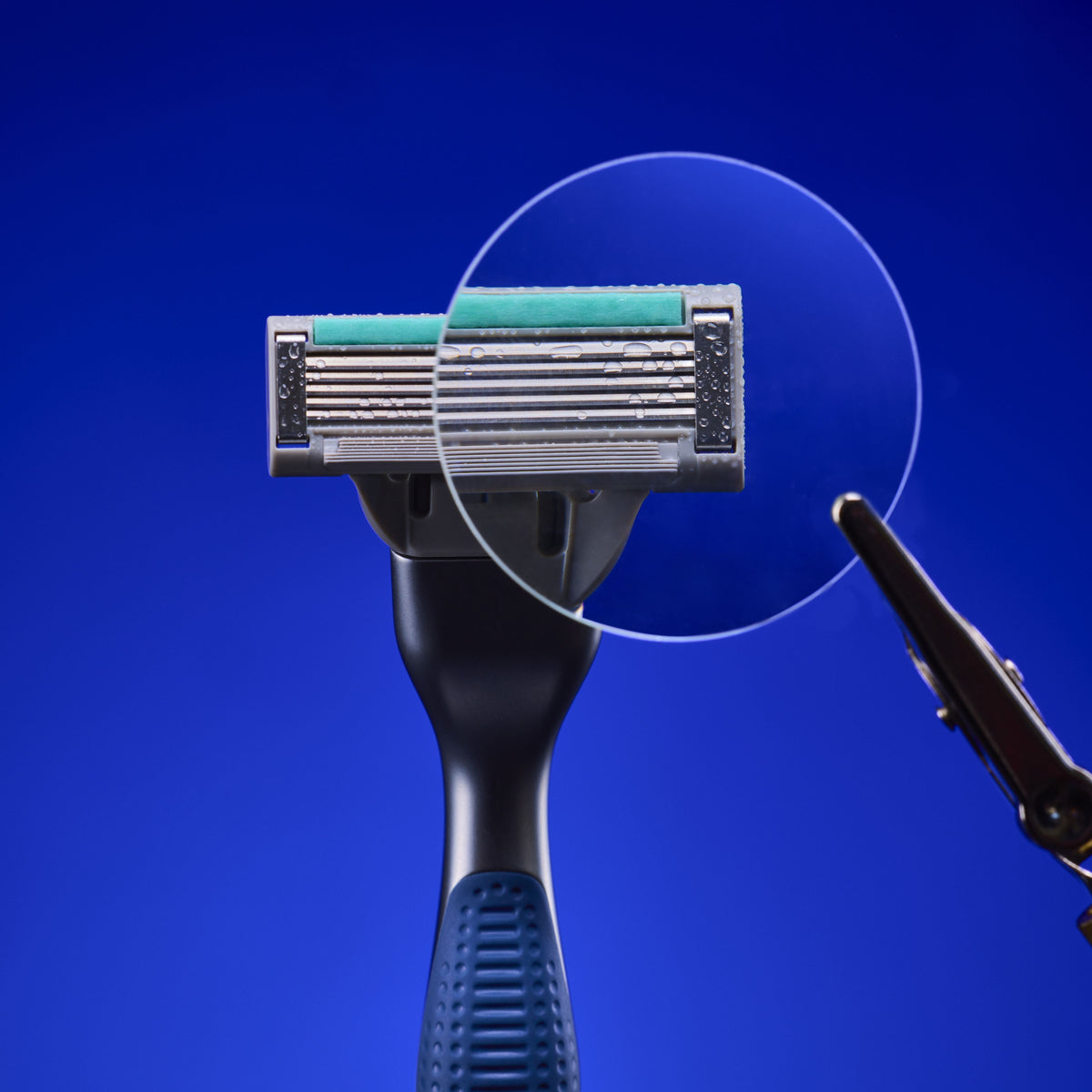 A close-up of a multi-blade razor with a dark handle and metallic head, shown against a solid blue background with a circular transparent overlay highlighting the blade area.