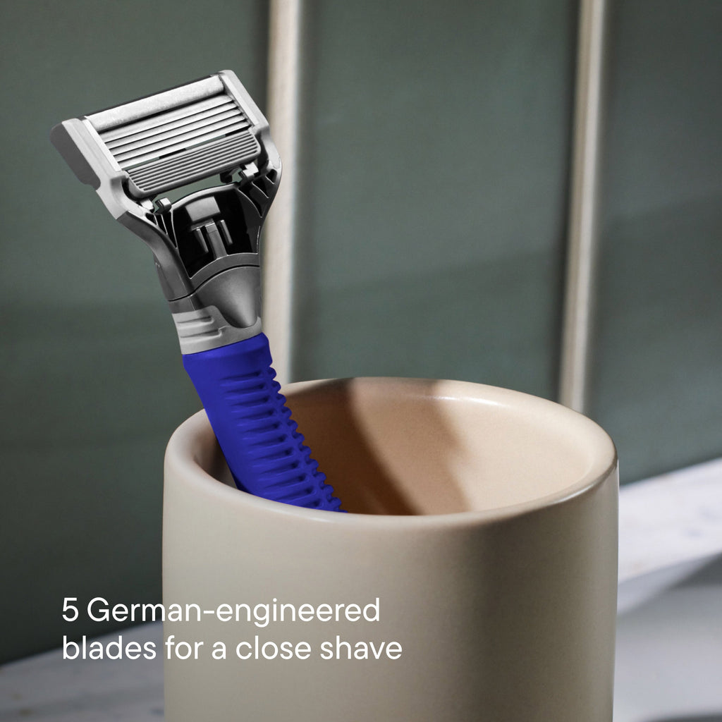 Shaving razor with blue handle in a beige cup on a blurred bathroom background
