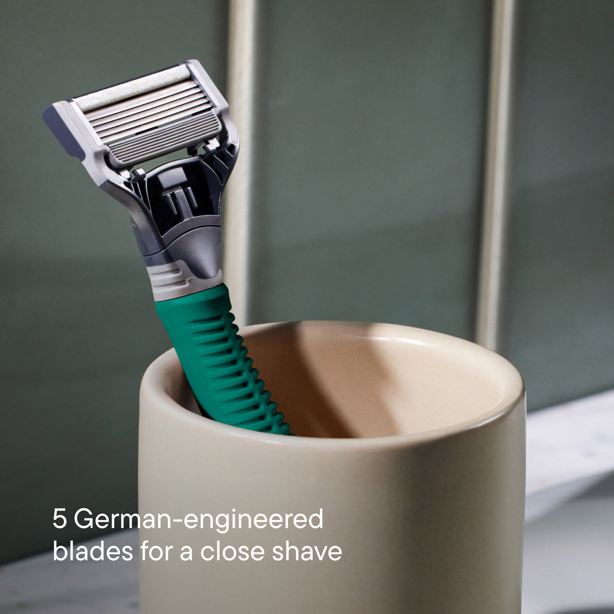 Shaving razor with green handle in a beige cup on a blurred bathroom background